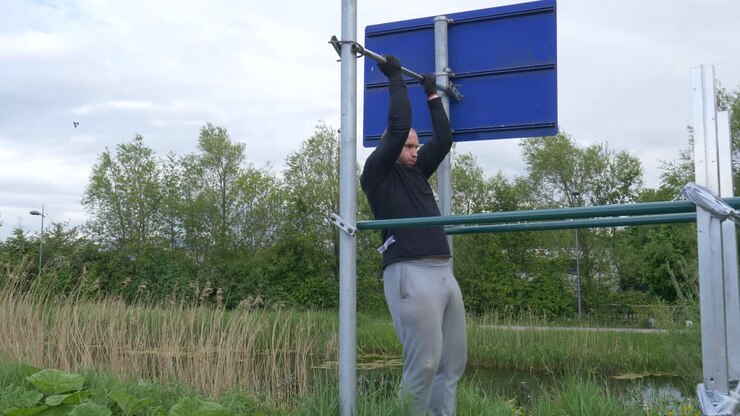Uomo che fa sport eseguendo trazioni alla sbarra su sbarre orizzontali fai-da-te - inquadratura ampia