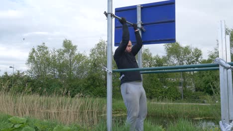 man goes in for sports doing pull-up exercises on diy horizontal bars - wide shot