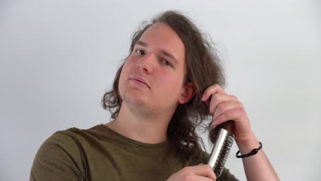 el primer plano de un joven feliz de piel blanca peinándose el cabello rubio con la mano derecha y usando una camiseta verde de fondo blanco