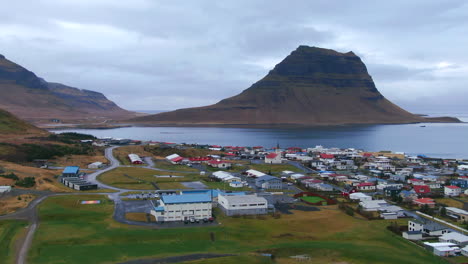 Fesselnde-Luftaufnahme-Einer-Küstengemeinde-In-Island-Mit-Bergen-Im-Hintergrund,-Kirkjufell-Berg-In-Der-Nähe-Von-Grundarfjordour