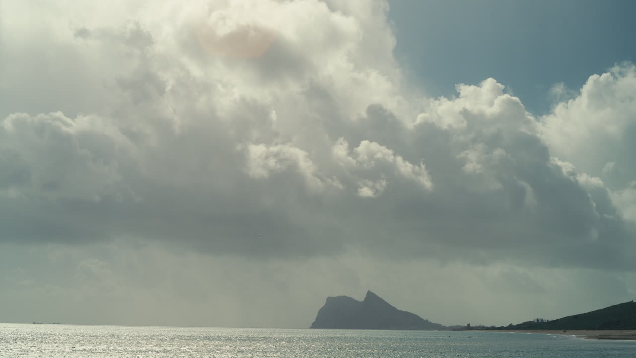 Dramatic storm clouds and patches of blue sky above the Rock of Gibraltar with sunlight reflecting on the calm sea