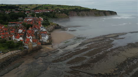 establishing aerial drone shot of robin hoods bay on misty morning at low tide