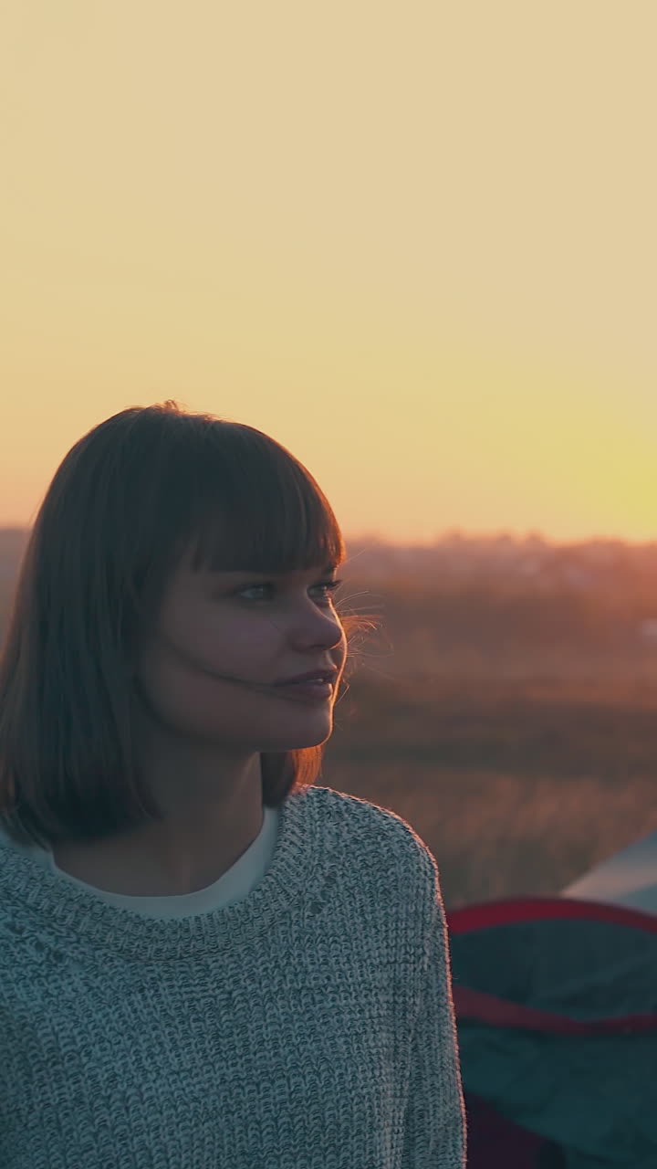happy girl talks with boyfriend near blue tent and friends in tourist camp in warm autumn evening at sunset on horizon