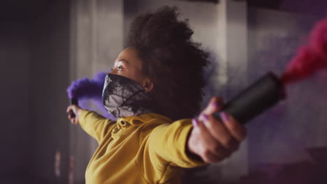 biracial woman holding blue and purple flares standing in an empty building