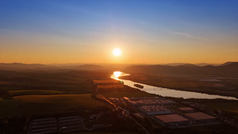 River sunset view over a rural landscape. Golden sunlight reflects on the river as the day ends, illuminating fields and mountains under a clear sky