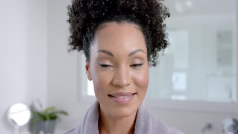 portrait of happy biracial woman in bathrobe in bathroom, slow motion