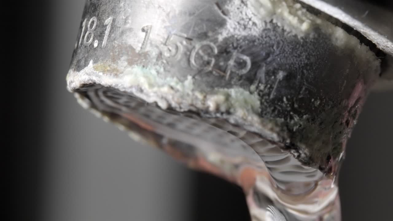 A close-up view of water flowing from a sink, with visible limestone buildup around the edges.