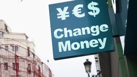 a currency exchange sign shows the message 'change money' with symbols for currencies like japanese yen, us dollar, and euro on a retail commercial street in madrid, spain