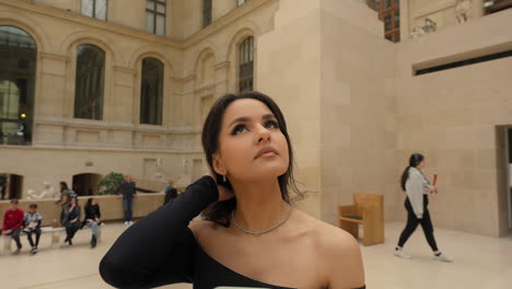 portrait of a beautiful elegant young brunette woman wearing a black dress, looking at the louvre museum