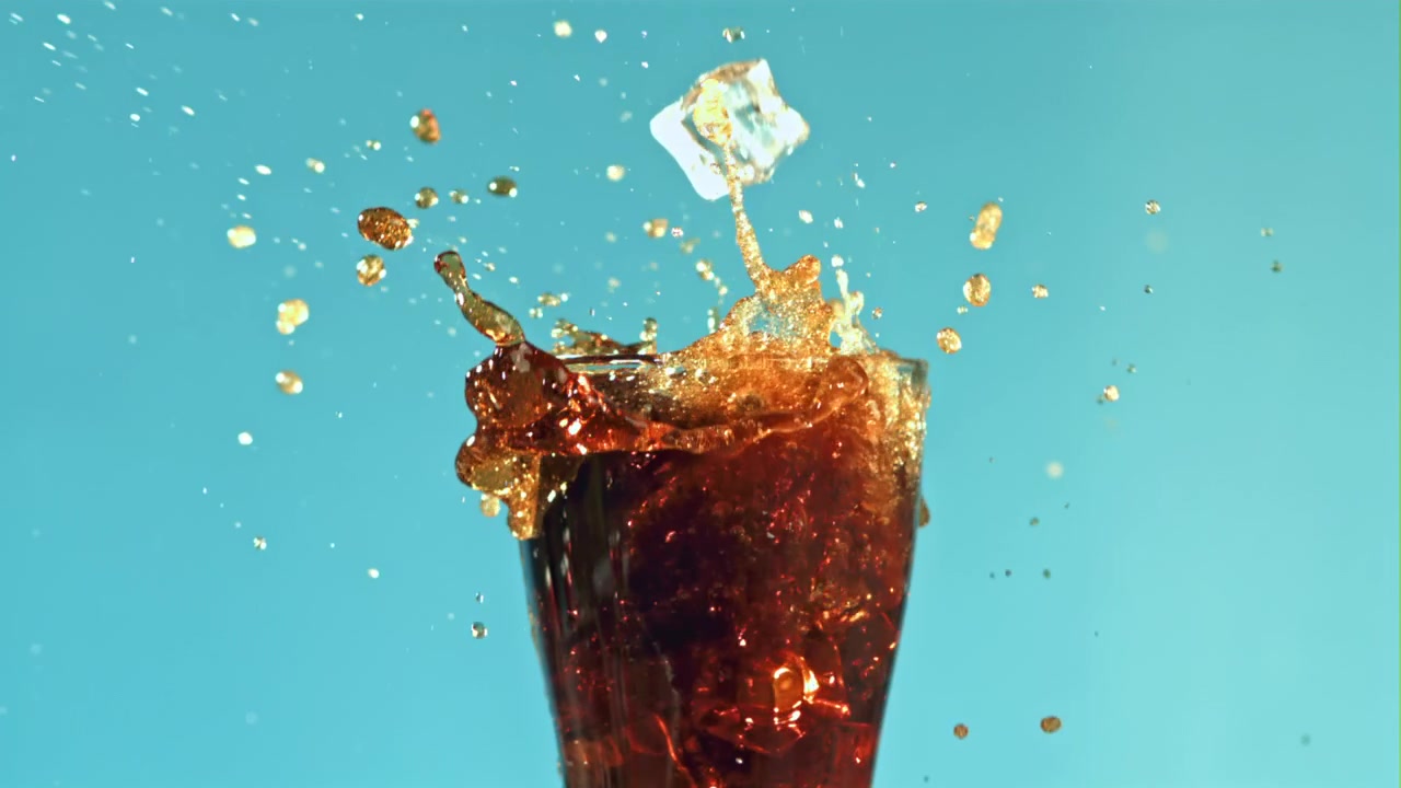 Cubetti di ghiaccio che cadono e schizzano in un bicchiere di cola