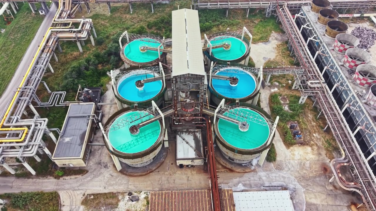 View of a large industrial facility with circular tanks filled with bright blue liquid during daytime