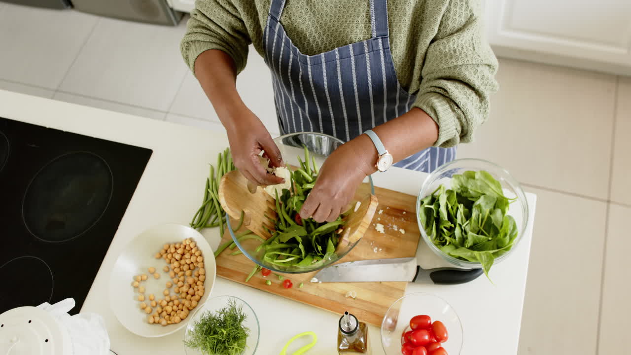 African american senior woman preparing salad in sunny kitchen, slow motion