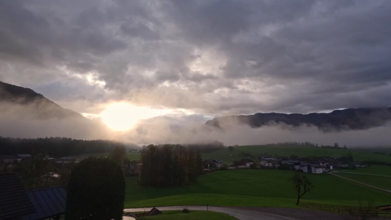 A serene sunset illuminates a valley with thick mist rolling through the landscape. Time lapse of a sunset on a cloudy morning with mountains.