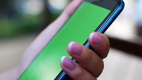 a woman is sitting in a cafe with a smartphone in her hands with a green screen mockup. the girl actively uses the phone for her own purposes. content, videos, blogs.