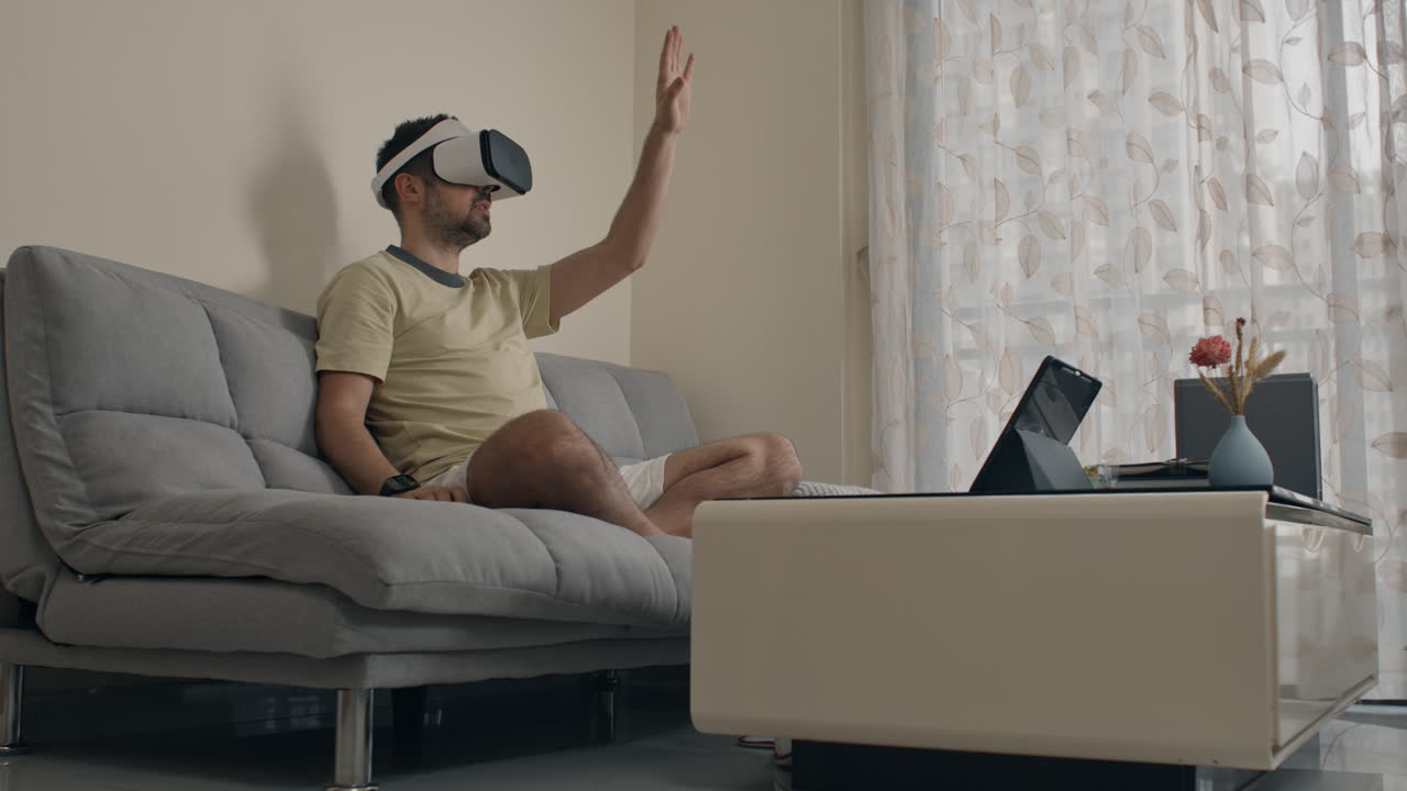 Man operating digital interface with VR headset while sitting on couch in living room