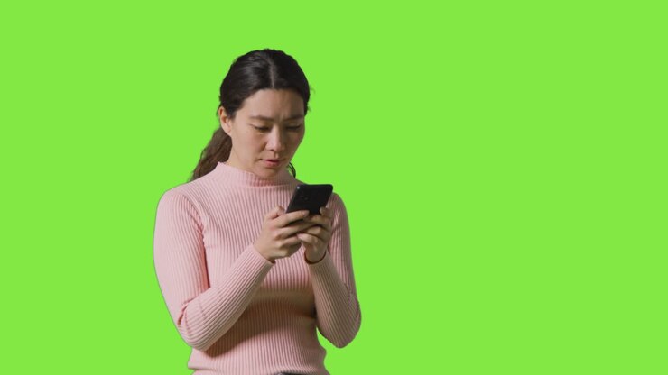 Studio Shot Of Woman Checking Mobile Phone And Getting Disappointing News Message Against Green Screen