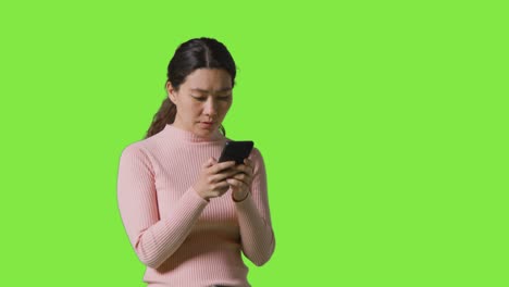 Studio-Shot-Of-Woman-Checking-Mobile-Phone-And-Getting-Disappointing-News-Message-Against-Green-Screen