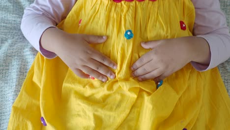 niño con vestido amarillo con las manos en el estómago