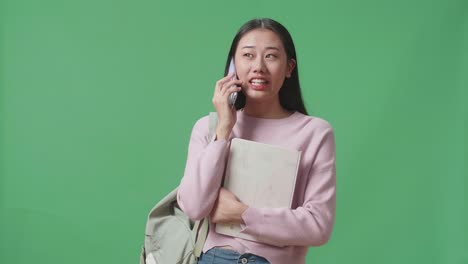 아시아 여학생이 녹색 스크린 스튜디오에서 휴대전화로 이야기하고 있습니다.
