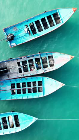 aerial vertical top down of wooden blue fishing boat floating on turquoise ocean sea water calm and relaxing vacation concept drone footage