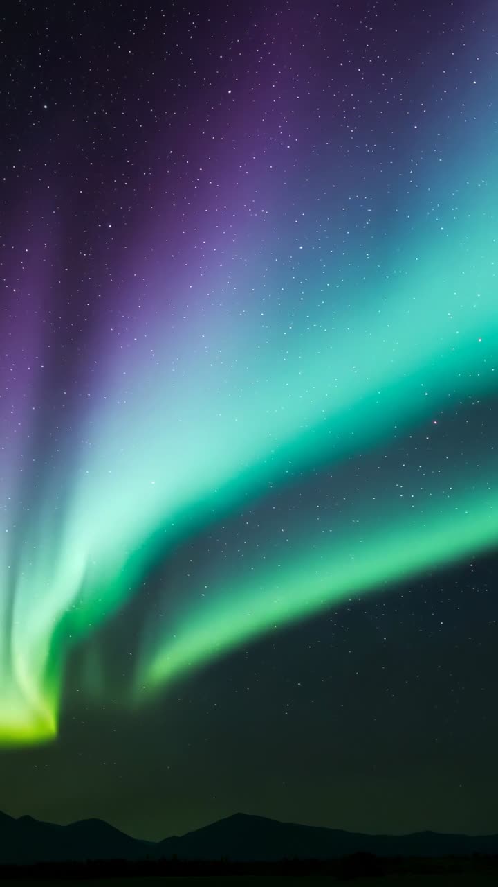 Vertical video: Emerging faint green aurora arc twisting and pulsing violet waves over mountains