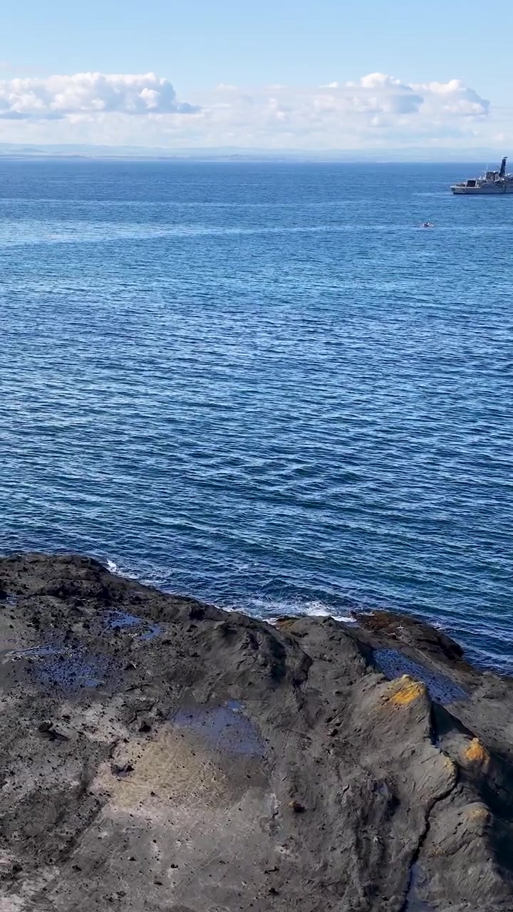 Pan Vertikal ke Atas dari Pantai Berbatu ke Laut Biru dengan Kapal di Kejauhan
