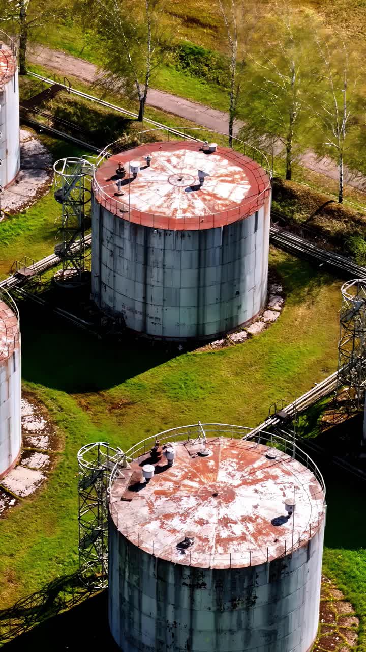 Vertical aerial of rusty circular industrial silos in green open area with road access
