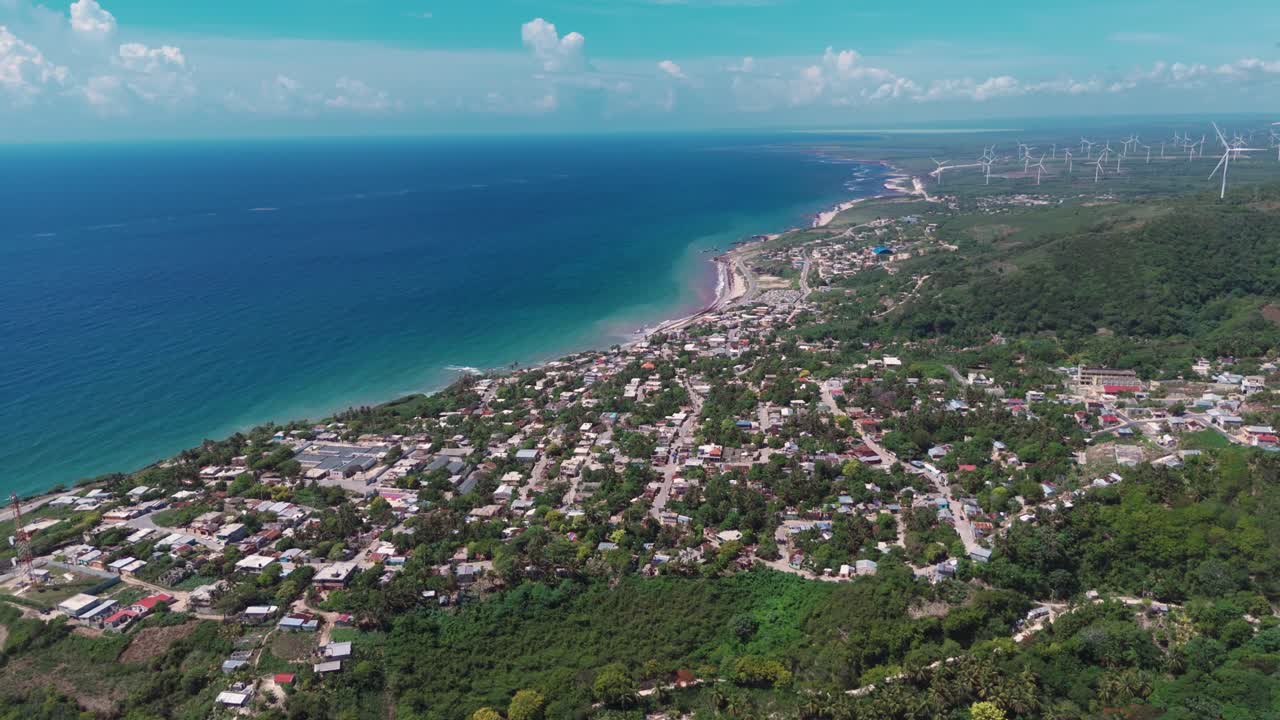 Wide aerial of coastal town Enriquillo and Los Cocos wind farm on green hills by Caribbean Sea, Barahona, Dominican Republic