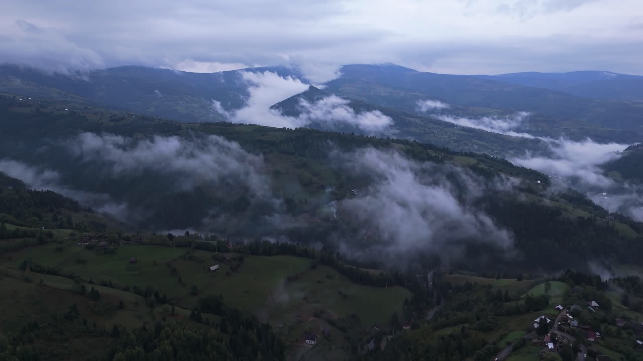 Aerial drone view of Mătișești village in Romania with clouds rolling over the forested hills and valleys of the Apuseni Mountains, creating a dramatic and moody post-rain atmosphere