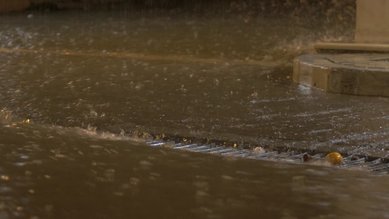 Torrential rainfall flowing down street into drain