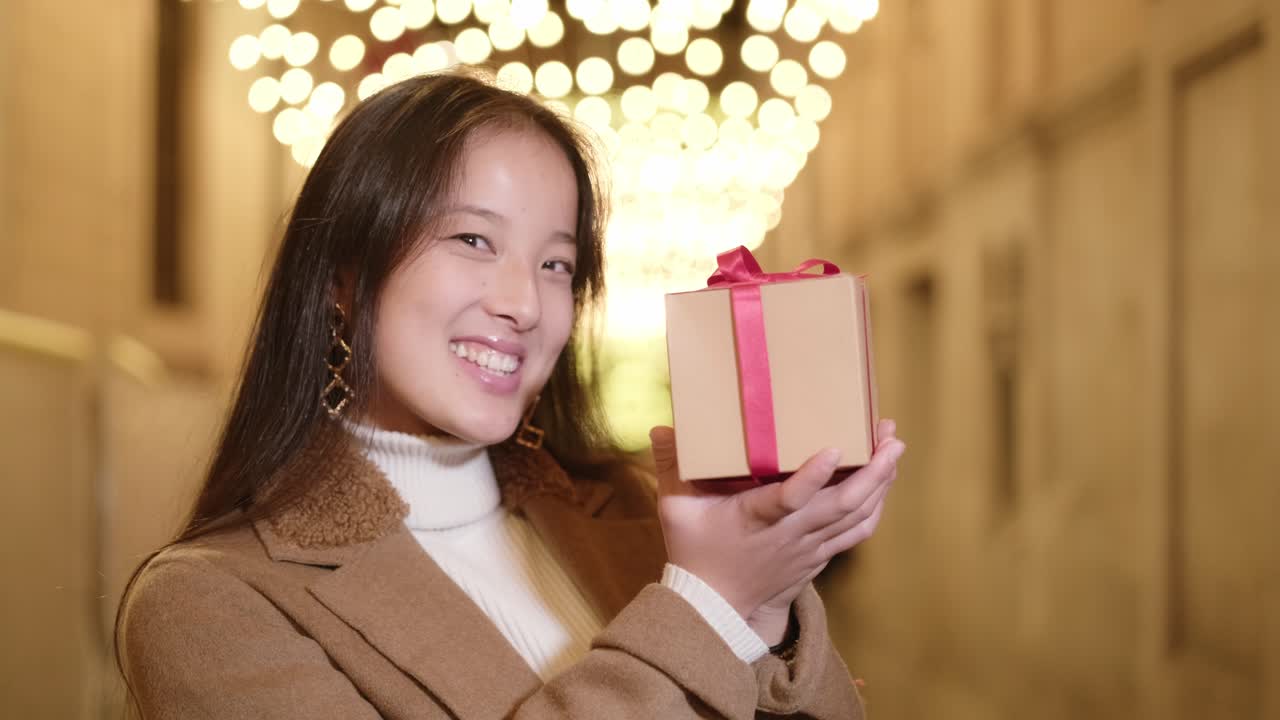 Young Asian woman smiling with a gift in a city tunnel