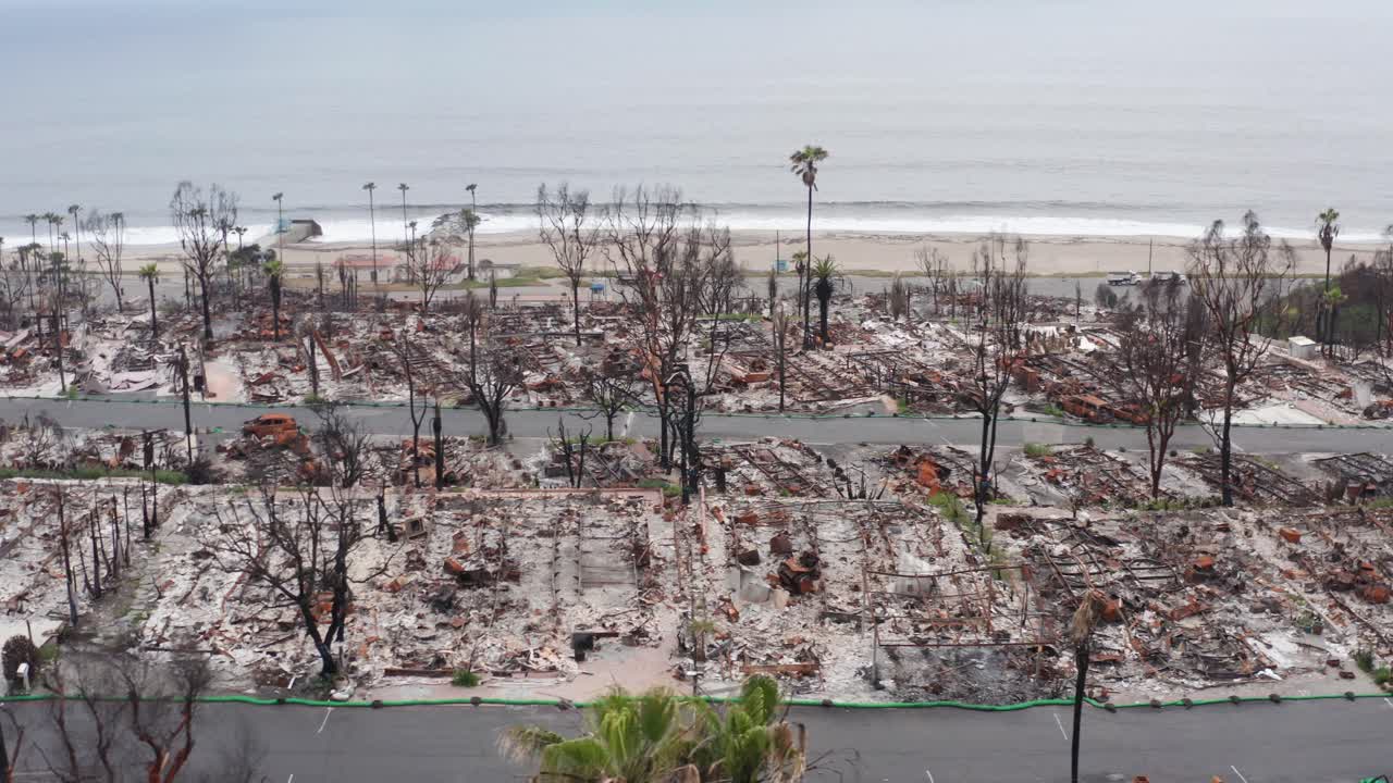 Aerial low dolly shot of beachfront charred mobile homes after the Palisades Fire in Los Angeles, California. 4K