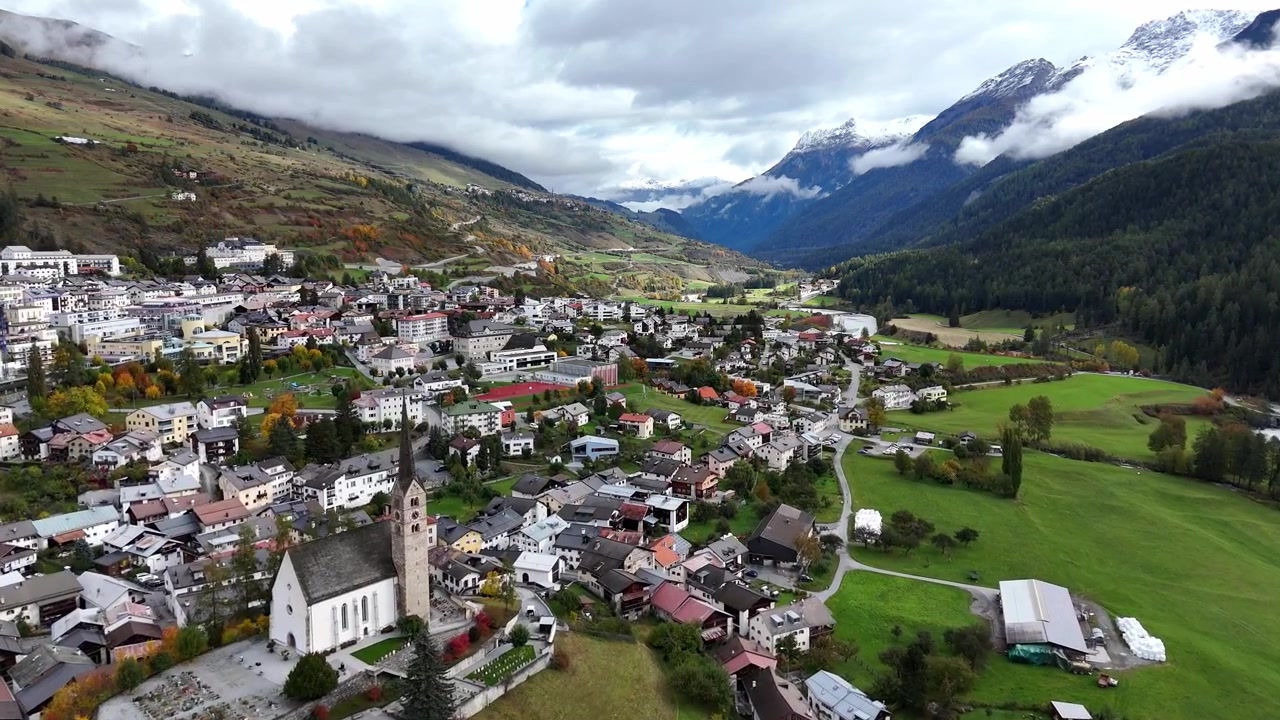 Luftfoto av Scuol, Sveits, som viser en pittoresk fjellandsby omgitt av grønne åser.