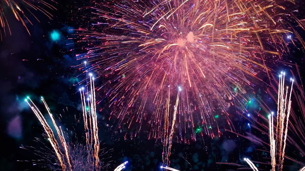 Vibrant fireworks burst in a night sky, captured from a low-angle, creating a celebratory