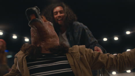 joven con máscara de caballo divirtiéndose sentado en el carrito de compras amigos disfrutando de una loca fiesta en la azotea por la noche celebrando juguetón el fin de semana
