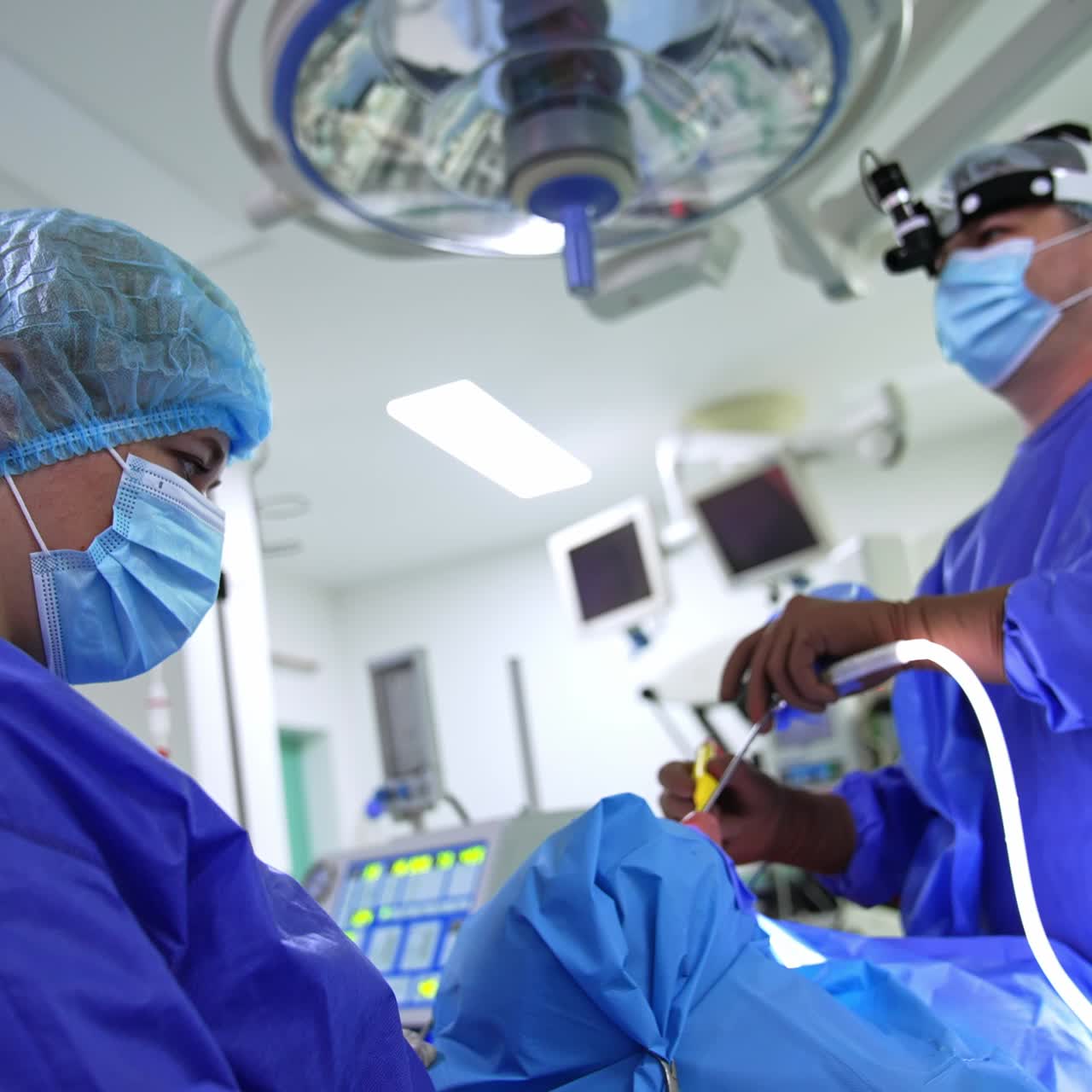 Female nurse in uniform, mask and cap looks at work of surgeon. Male doctor uses tools in nasal cavity following the monitor
