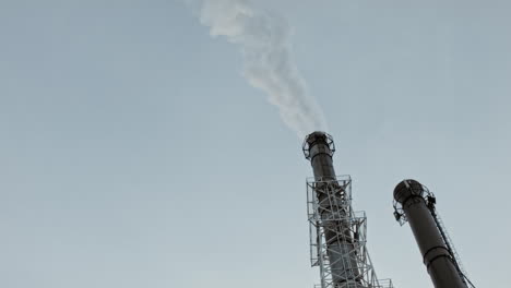 industrial factory pipe over a blue sky with loads of smoke from ground