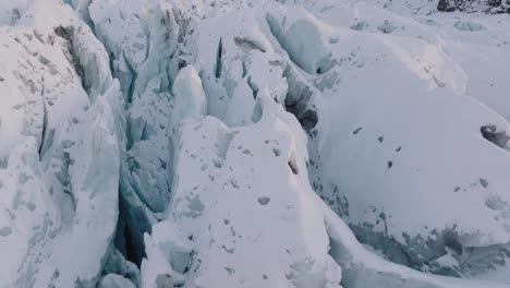 aerial view over irregular ice formations in falljokull glacier covered in snow, iceland, during sunset