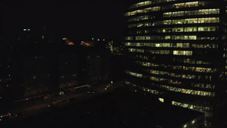 aerial night shot of a tall office, financial building as people working late with lights on in the offices, light traffic on the roads