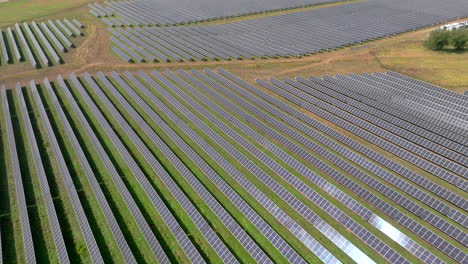 Aerial-pan-up-view-of-large-solar-farm-with-many-rows-of-solar-panels-creating-green,-renewable-energy-to-replace-fossil-fuels-and-to-power-clean-transition-to-fight-climate-change