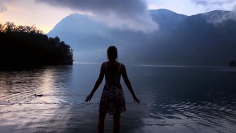 this is a 4k shot of a beautiful girl standing on a footbridge in front of a mystical lake in slovenia