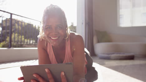 A-senior-African-American-woman-is-lying-on-her-stomach,-using-tablet