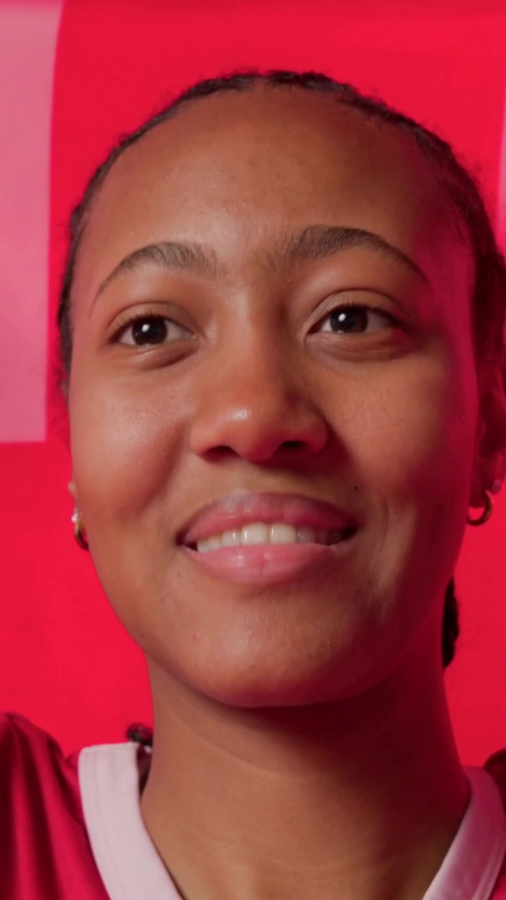 Video verticale: Donna sorridente che si muove a destra, con panoramica della telecamera, mostrando una parete rossa e una maglietta sportiva, spazio per il testo.