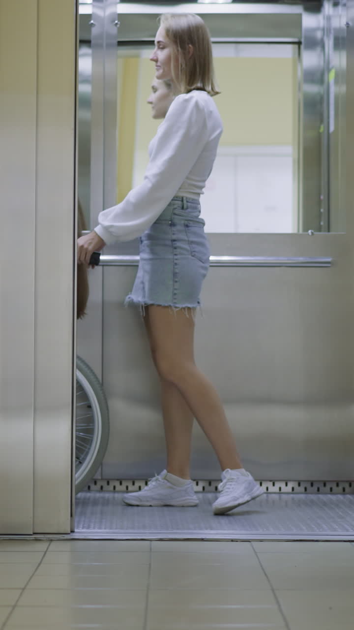 Young woman pushes button to close door of modern elevator. Female person helps best friend with disability get to doctor office in hospital