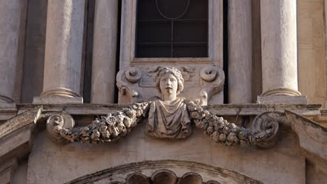 Close-up of a sculpted bust and floral garland detail on the Trevi Fountain in Rome, Italy, showcasing ornate baroque stonework and classical architecture in daylight.