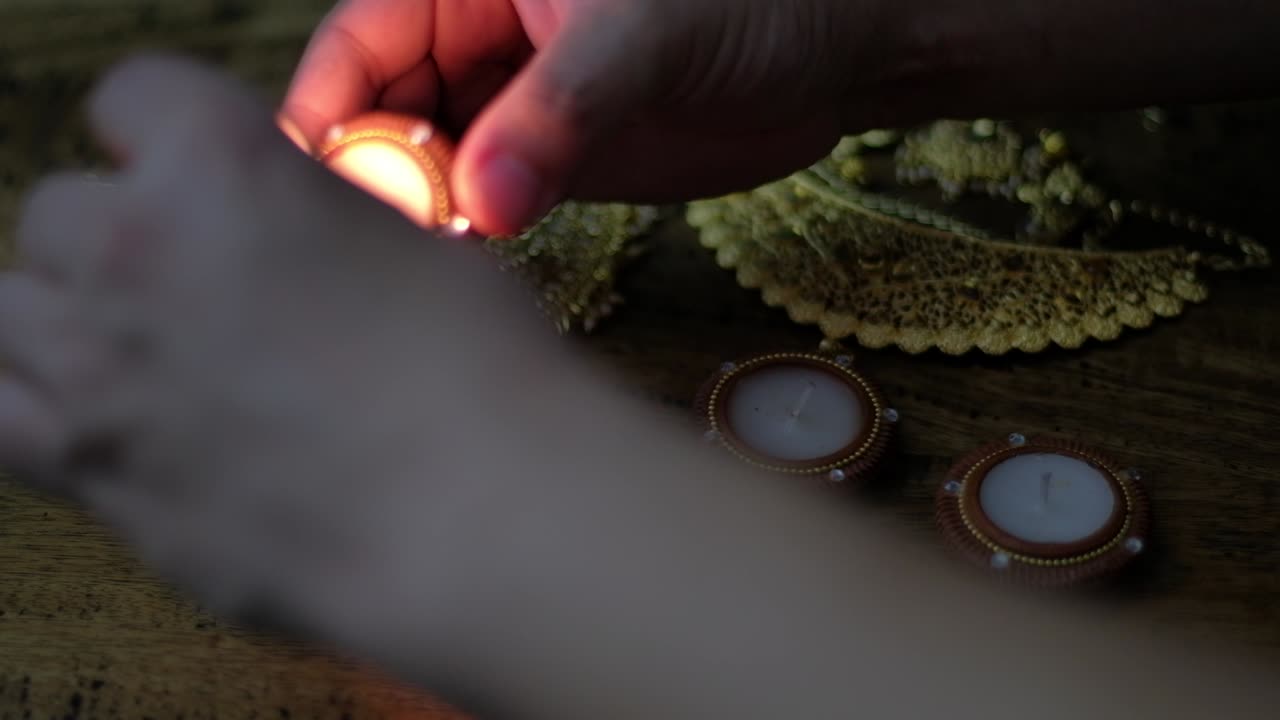 Close-up of human hands lighting four wax light diya candles with golden jewellery for worship of wealth, prosperity and Laxmi during the Hindu festival of lights or Diwali.