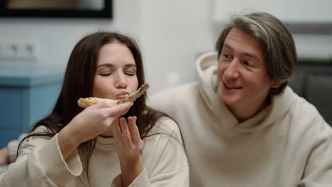 Young-woman-eats-pizza-and-offers-bite-to-boyfriend,-they-feeling-so-happy
