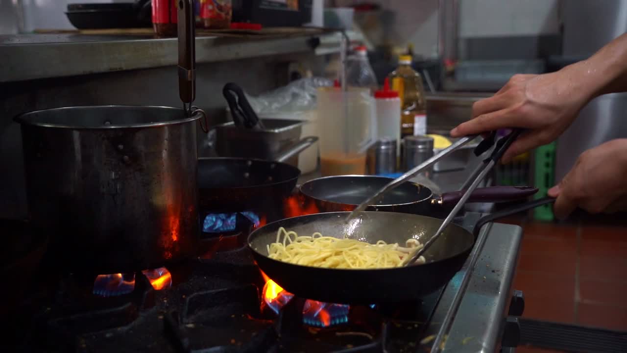 Chef cooking veg aglio olio pasta, stir fried spaghetti with mixed mushrooms, garlic and olive oil, flipping the pan and mixing the ingredients in slow motion
