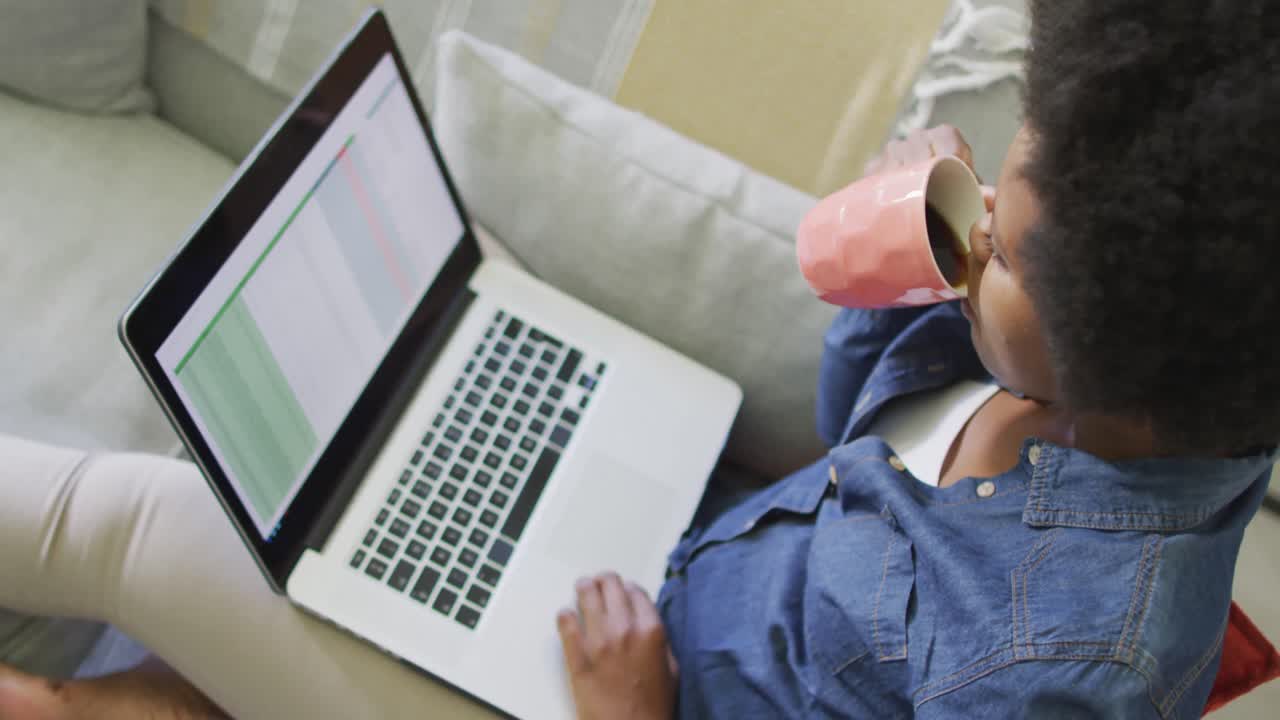 feliz mujer afroamericana sentada en el sofá, usando una computadora portátil