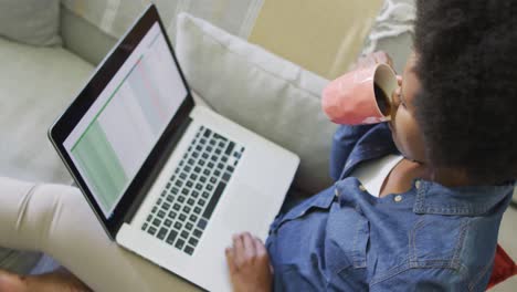 happy african american woman sitting on sofa, using laptop